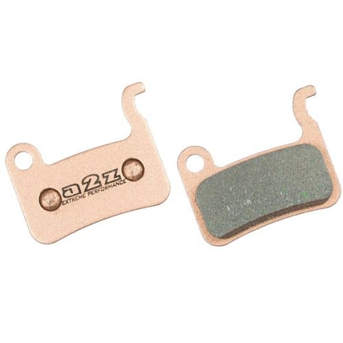 Två bromsbelägg av metall, det ena med en platt metallplatta med texten "Q2X Extreme Performance" och det andra med en yta av friktionsmaterial fäst på en liknande platta.