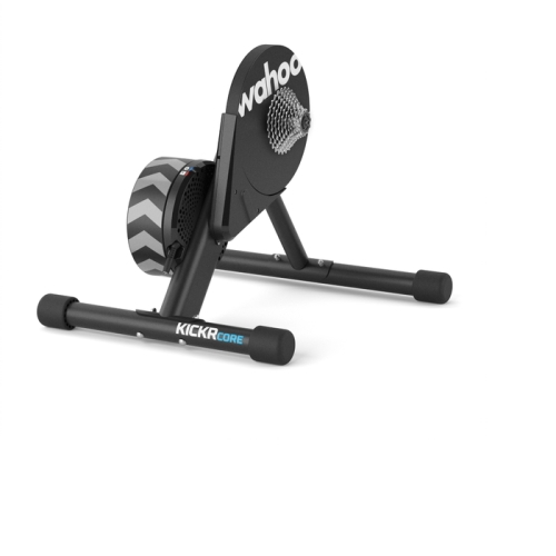 En stationär cykelmaskin för inomhusbruk märkt "Wahoo KICKR CORE" med svart ram, chevronmönster på svänghjulet och kassett för att fästa en cykel.