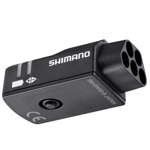 En svart Shimano elektronisk cykelkomponent med fyra cirkulära portar, en knapp och tryckta etiketter, inklusive CE-märket och "SW-EW50B JAPAN". Komponenten har en kompakt, rektangulär form.