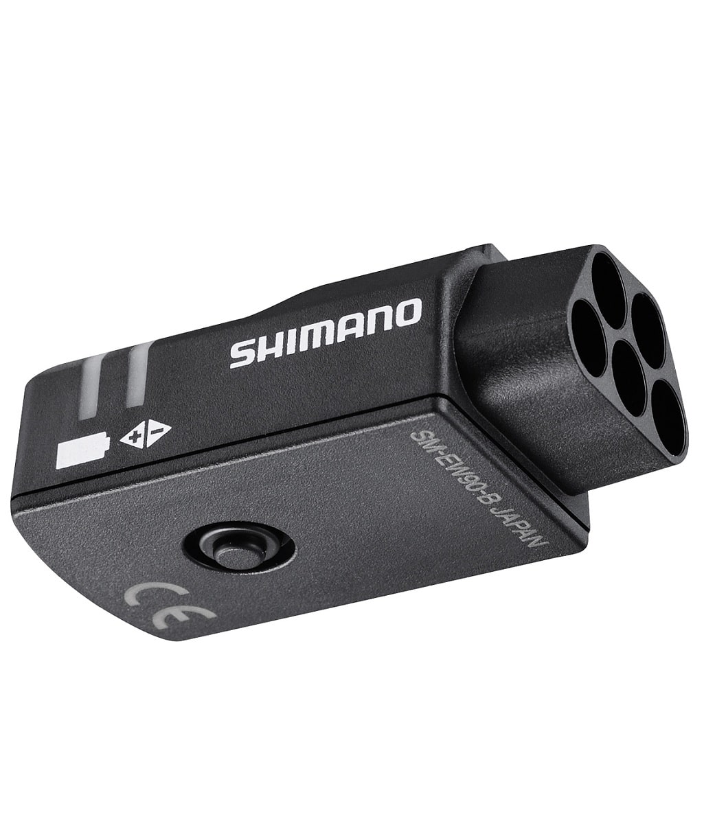Kopplingsbox-5-Portars.jpg En svart Shimano elektronisk cykelkomponent med fyra cirkulära portar, en knapp och tryckta etiketter, inklusive CE-märket och "SW-EW50B JAPAN". Komponenten har en kompakt, rektangulär form.