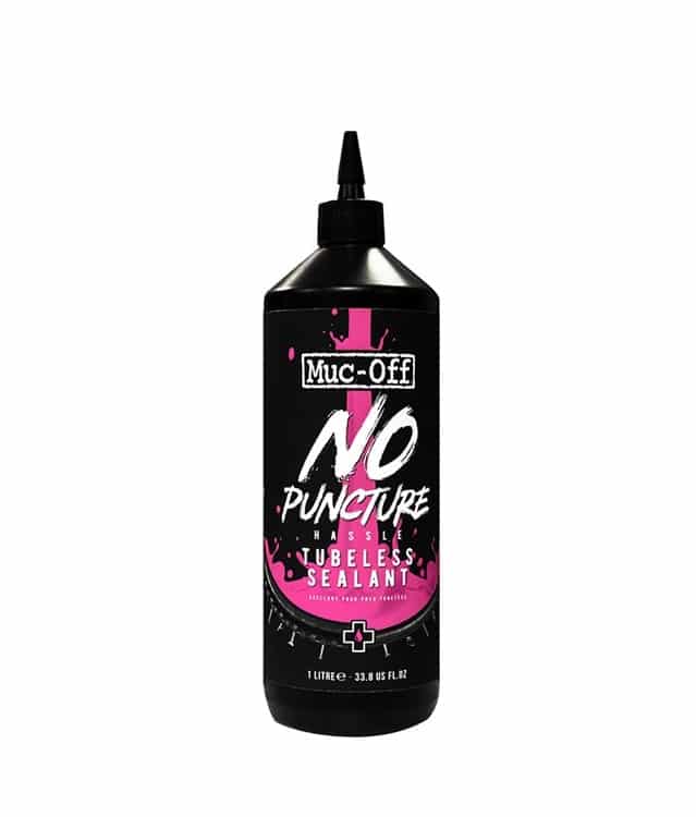Muc-Off-No-Puncture-1L.jpg En svart 1-litersflaska med Muc-Off No Puncture Hassle Tubeless Sealant med ett spetsigt applikatorlock. Etiketten har rosa och vit text och grafik på en svart bakgrund.