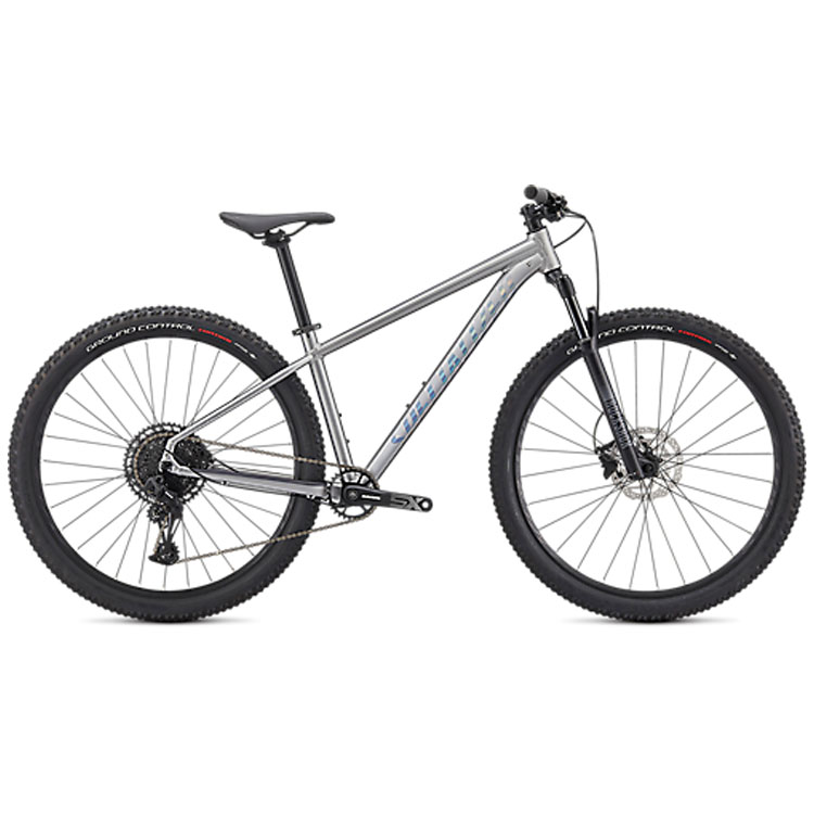 Rockhopper-Expert-silver.jpg En silverfärgad mountainbike med svart styre, sadel och stora knobbiga däck, visad i profil mot en vit bakgrund. Cykeln har en framgaffel med fjädring och inga synliga tillbehör.