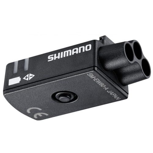 En svart Shimano elektronisk cykelkomponent med tre cirkulära portar, en central knapp och vit textmärkning på sidan. Enheten har symboler och en CE-märkning på ytan.