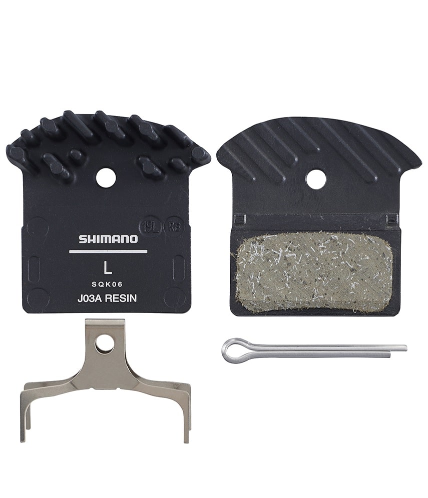 Shimano-J03A.jpg En uppsättning Shimano J03A skivbromsbelägg av harts, inklusive två bromsbelägg med kylflänsar, en metallfjäder och en silverfärgad fäststift, allt arrangerat på en vit bakgrund.