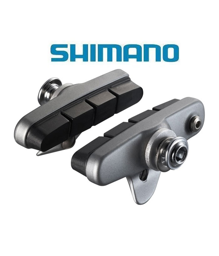 Shimano-Ultegra-6700-bromskloss-med-utbytbara-belagg-till-55mm-bromssko.jpg Två Shimano-bromsbelägg för cyklar visas mot en vit bakgrund med den blå SHIMANO-logotypen ovanför dem. Beläggen har en baksida av metall och bromsytor av svart gummi.
