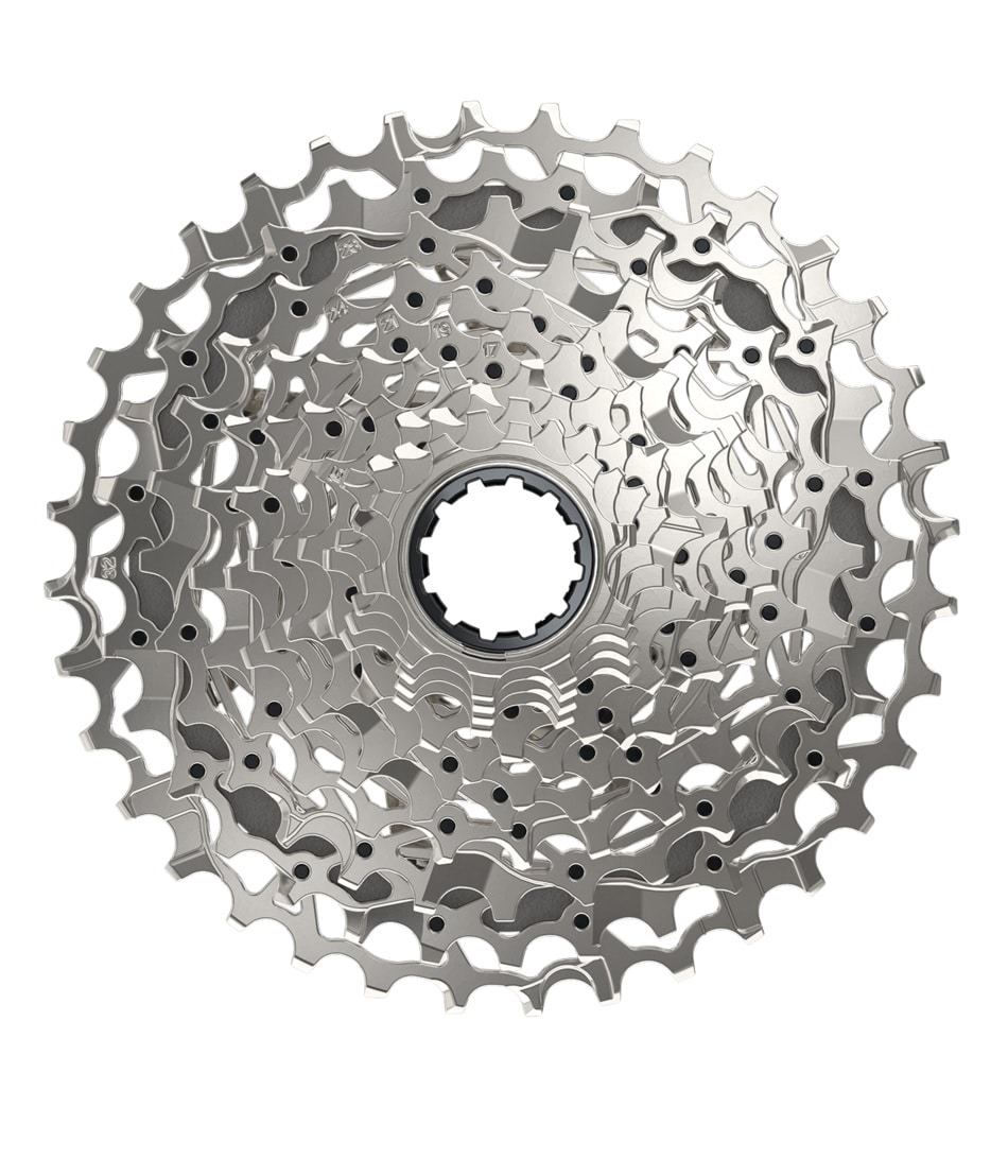 XG1250-Kassett.jpg En närbild av en silvrig cykelkassett med flera kedjehjul, arrangerade i ett cirkulärt mönster, isolerad mot en vit bakgrund.