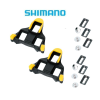Två svarta och gula Shimano-cykelklämmor med sex metallbultar och sex rektangulära brickor visas på en vit bakgrund, med den blå Shimano-logotypen ovanför dem.