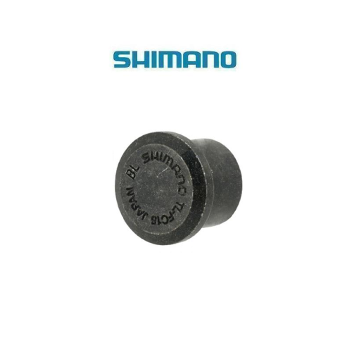 En liten svart cylindrisk Shimano-komponent, troligen en gummi- eller plastplugg, visas mot en vit bakgrund med den blå Shimano-logotypen ovanför. Pluggen är märkt med "SHIMANO", "JAPAN" och "Y4CR18000".