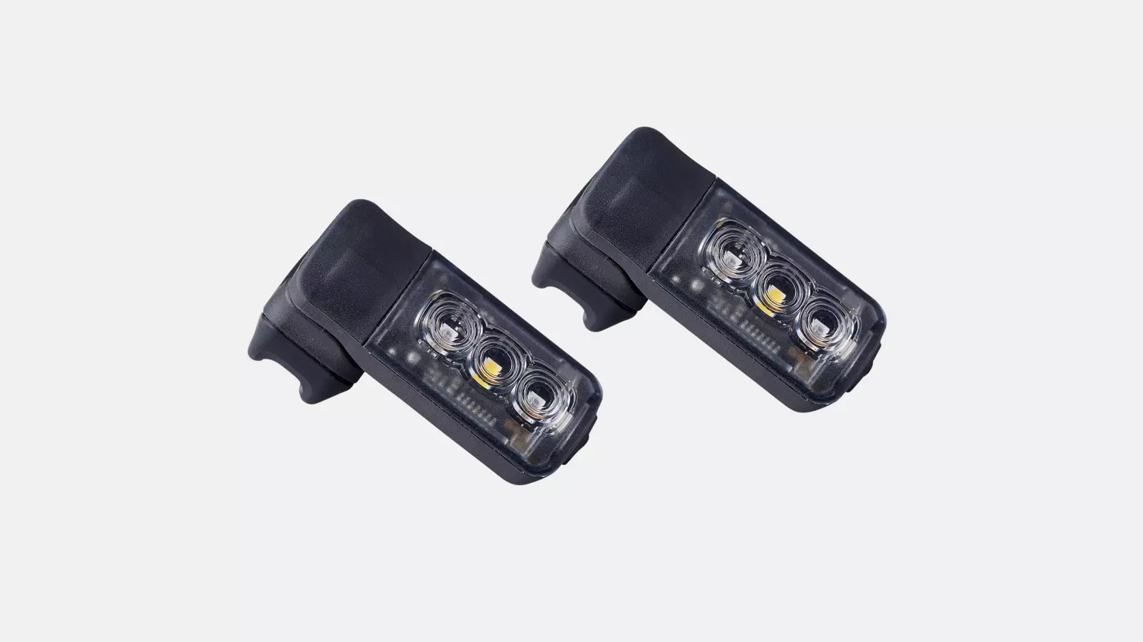 49119-400_LGHT_STIX-SWITCH-COMBO-HEADLIGHT-TAILLIGHT_HERO-2.webp Två svarta rektangulära cykellampor Specialized Stix Switch Fram/baklampa, var och en med tre synliga LED-lampor, avbildade på en vit bakgrund och vinklade något uppåt och åt höger.