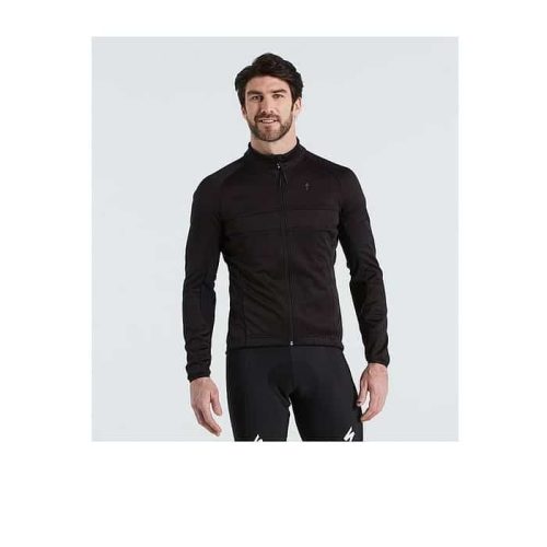 En man med kort mörkt hår och skägg är klädd i Specialized RBX Comp Softshell Jacket Men, en svart sportjacka med lång ärm och dragkedja, med svarta cykelshorts, och står mot en ljusgrå bakgrund.