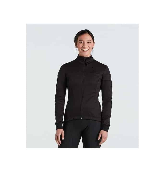 64422-3302.jpg En kvinna står vänd mot kameran, ler och bär Specialized RBX Comp Softshell Jacket Women i svart mot en vanlig ljus bakgrund.