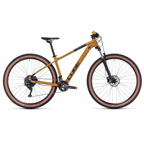 Sidovy av en mountainbike med guldfärgad ram, svart sadel, styre och ekrar samt däck med solbruna sidor. Cykeln har "CUBE"-märke på ramen och har framfjädring.