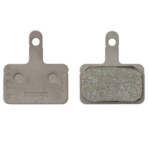 Två Shimano B05S resin skivbromsbelägg visas mot en vit bakgrund, en med bromsytan exponerad. Båda har en metallbärare med ett hål för montering.