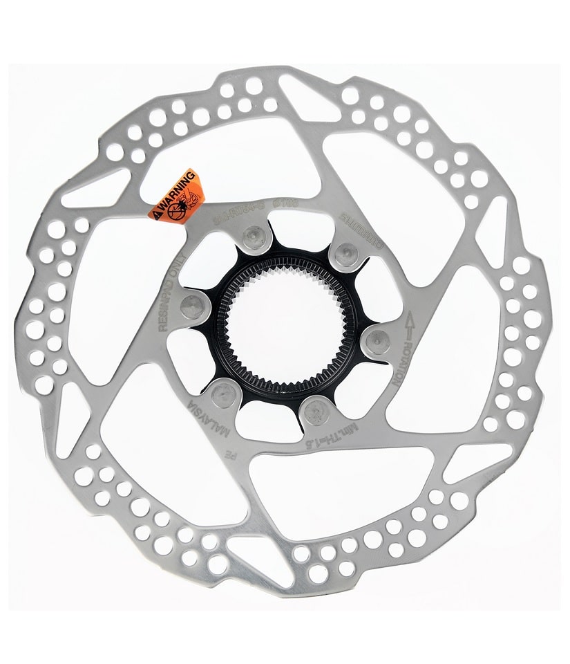 Bromsskiva-160mm-Center-Lock-SM-RT54-utan-lasring.jpg Närbild av en Shimano Alivio SM-RT54S bromsskiva för cykel med centerlock-infästning. Skivan är silvrig med hålmönster och en orange varningsetikett. Ljuset är jämnt och framhäver detaljerna.