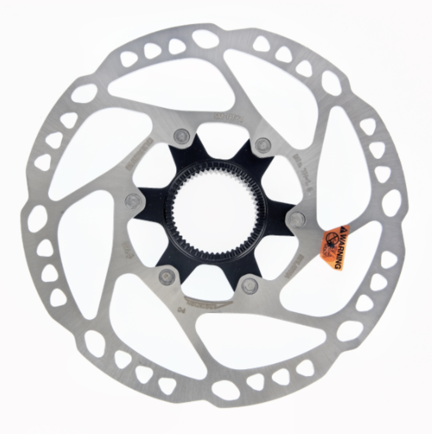 Bromsskiva Shimano SM-RT64 Närbild av en Shimano Deore SM-RT64 bromsskiva, centrerad mot en vit bakgrund. Skivan är av metall med en svart central nav och en orange varningsetikett.
