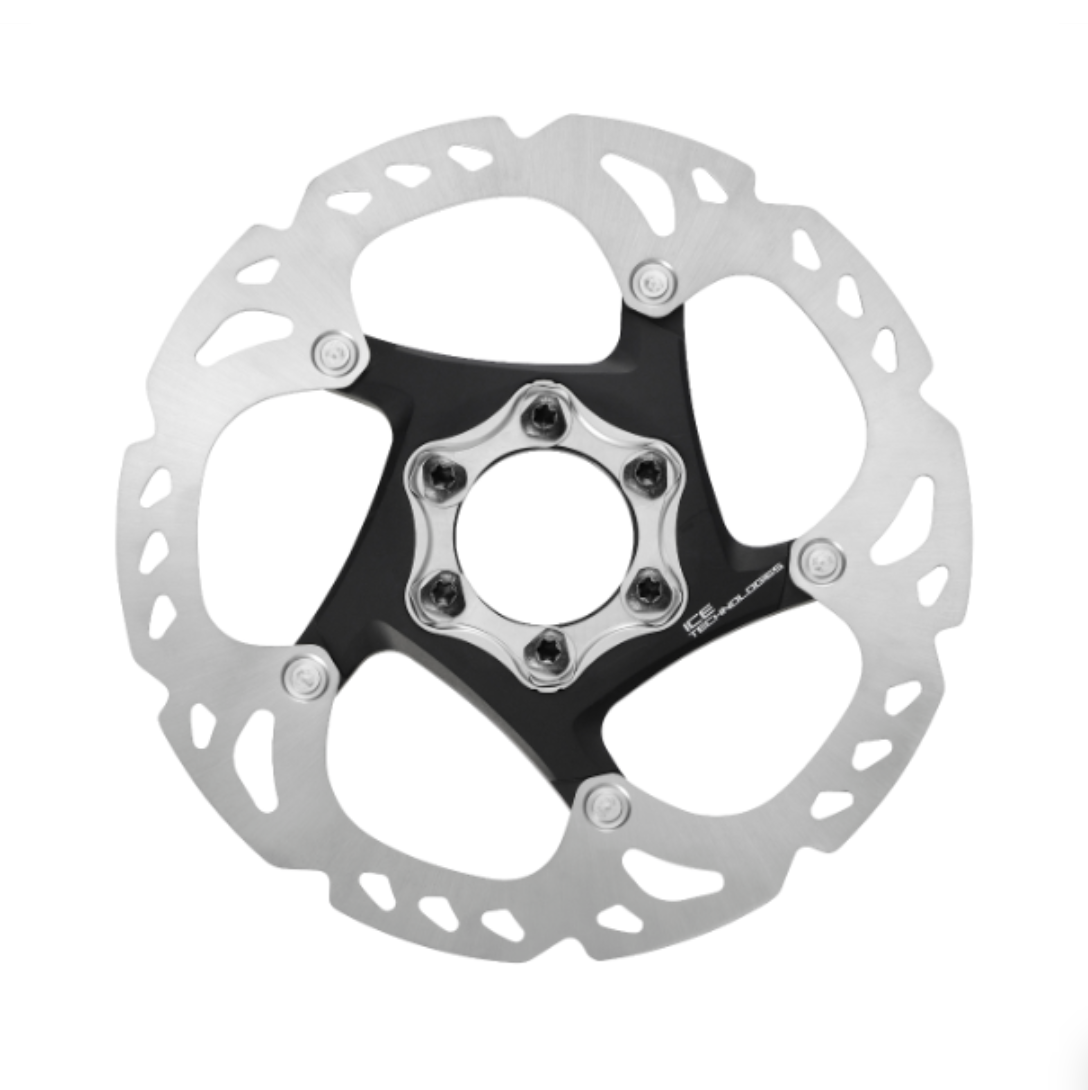 Bromsskiva XT SM-RT86 Bromsskiva Shimano XT SM-RT86 visas i detalj, med sin silverfärgade skiva och svarta centrum. Sex bultar håller enheten samman. Studioljus betonar skivans intrikata design.