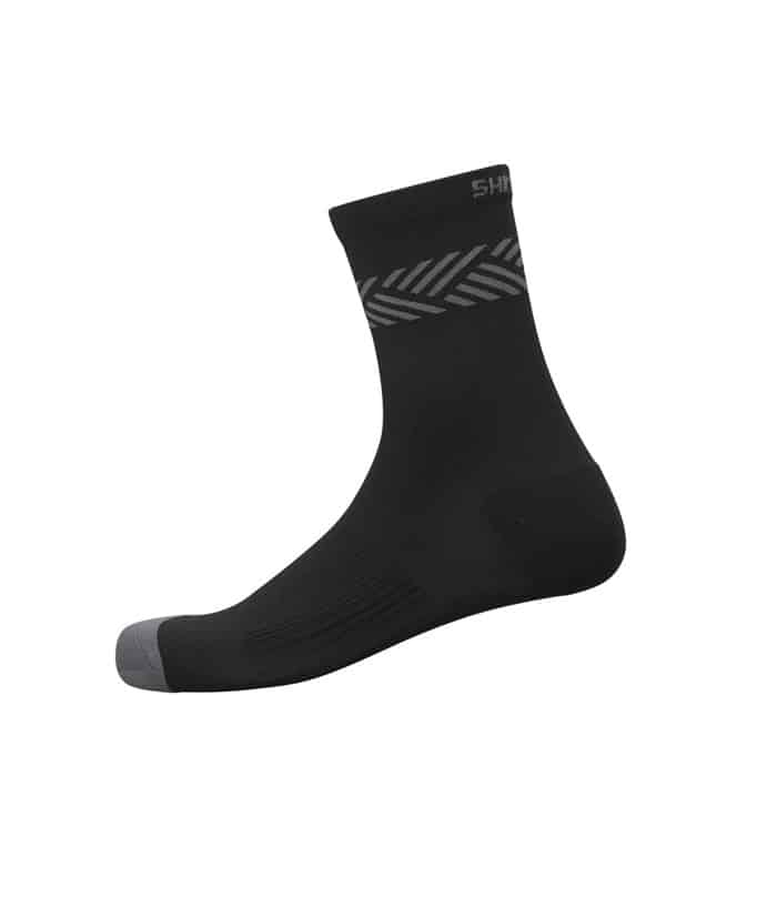 CW-SCBS-VS11U.jpg Shimano Original Ankle Sock är svart med grå tå och ett subtilt sicksackmönster nära toppen, tillverkad av smidigt, stretchigt material och visas mot en vanlig vit bakgrund.