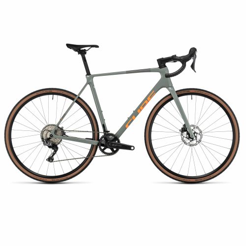En grå gravelcykel med orangefärgade detaljer visas i profil mot en vit bakgrund. Den har droppstyre, skivbromsar, svart sadel och däck med solbrända väggar.