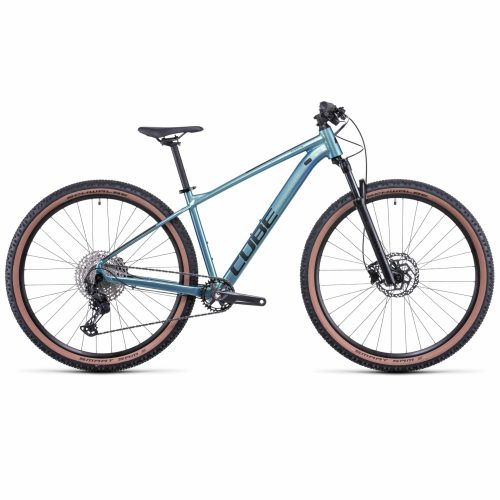 Blå MTB 27,5" Cube Attention SL, 1x12s mountainbike med hardtailram, framgaffel med fjädring, platt styre, skivbromsar och stora knobbiga däck med bruna sidor mot en vit bakgrund.