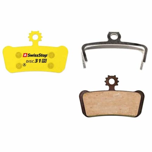 Närbild av Swissstop Disc 31 organiska skivbromsbelägg, inklusive en gul belägg, en fjäder och en belägg med träfärgad friktionsyta mot en ljus bakgrund.