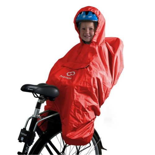 Ett leende barn med blå hjälm sitter på en cykelsadel, skyddad av Regnponcho Hamax - en klarröd regnponcho med huva som täcker både barnet och cykelsadeln.