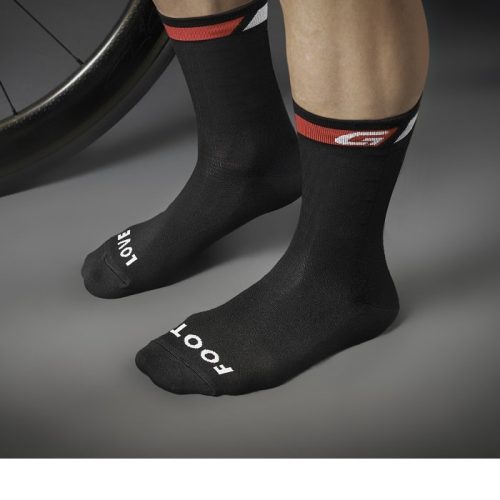 En person bär GripGrab Classic High Cut strumpor-svarta strumpor med röda och vita manschettränder. "LOVE" är tryckt på vänster tå, "FOOT" på höger. Ett cykelhjul syns delvis i bild.