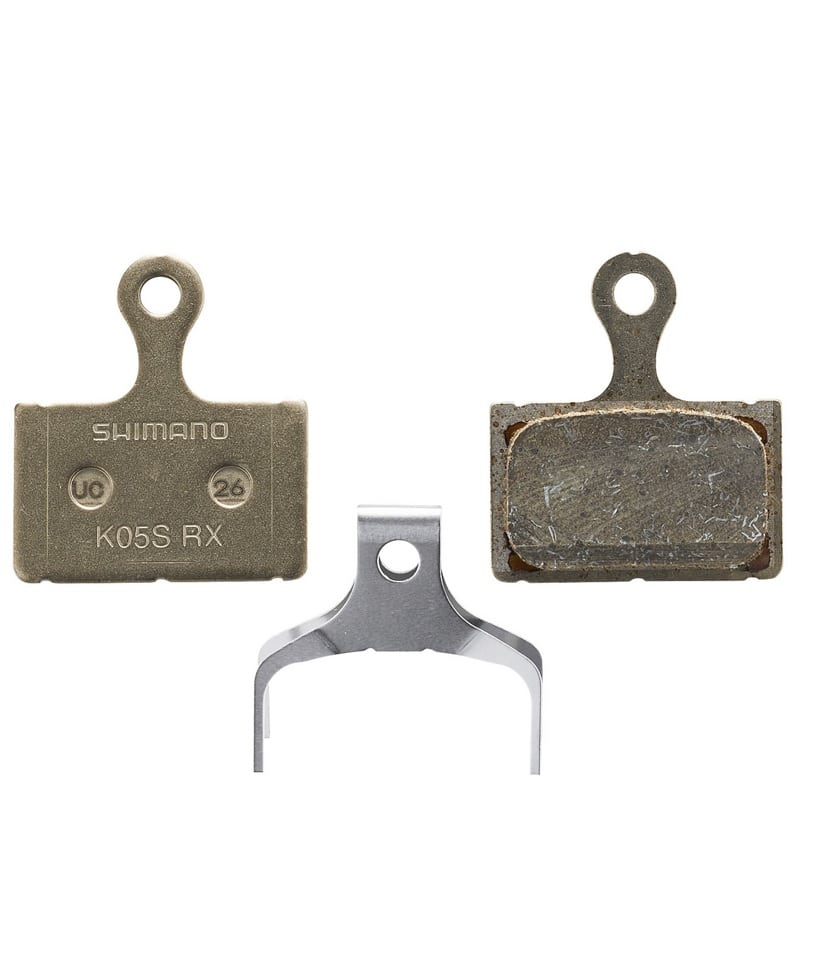 K05S-Resin.jpg Närbild av Shimano K05S resin skivbromsbelägg, både nya och använda, samt en fjäder, mot en neutral bakgrund. Jämnt ljus framhäver detaljer som text och material.