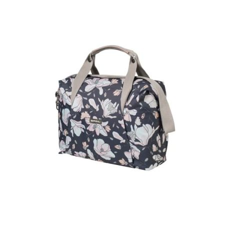 Cykelväska Basil Magnolia 18 liter är en rektangulär handväska med beige handtag och axelrem, med en mörk bakgrund med ljusrosa, vitt och blått blommönster.