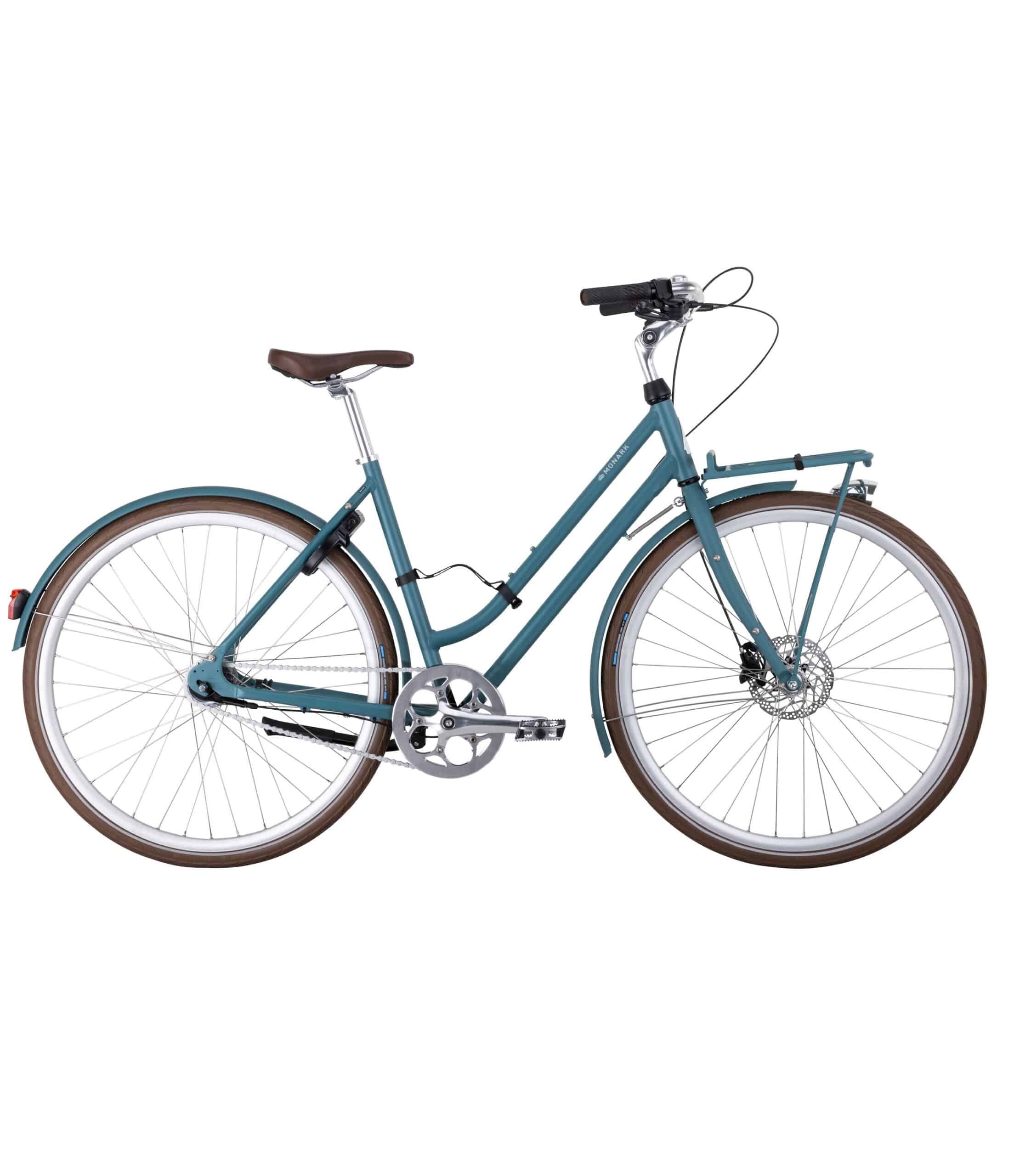 Monark-Karla-7vxl-51cm-bla-scaled-1.jpg En blå genomgående stadscykel med brun sadel och styrhandtag, fram- och bakskärmar, pakethållare och tunna landsvägsdäck, sedd från sidan mot en vit bakgrund.