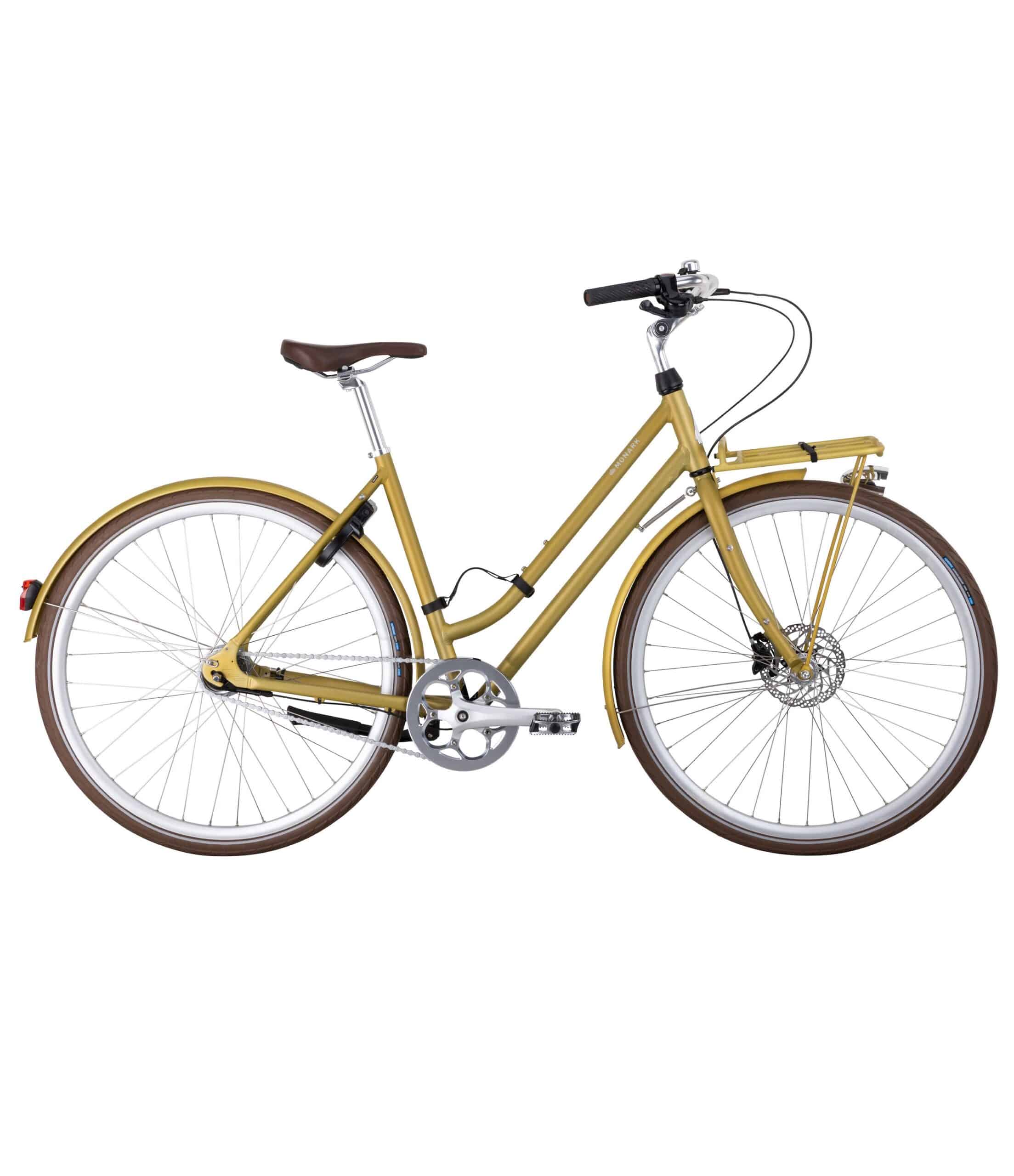 Monark-Karla-7vxl-51cm-secret-safari-scaled-1.jpg Damcykel Monark Karla 7s, 28" är en gul genomgående stadscykel med brun sadel och handtag, silverfärgade pedaler, pakethållare, tunna däck, skärm fram och bak samt skivbroms fram.