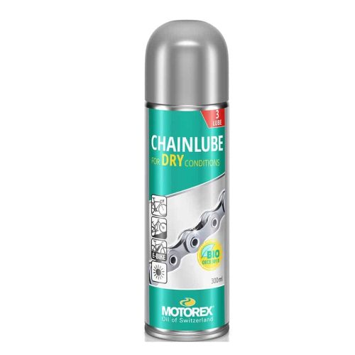 En detaljerad bild av en flaska Motorex Dry Lube kedjeolja, avsedd för torra förhållanden. Flaskans silverfärgade topp kontrasterar mot etikettens turkos och texten "CHAINLUBE". Belysningen framhäver produktens egenskaper och design.