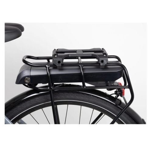 En närbild av Atran Velo Newrack Uni AVS-adapter - ett bakre cykelställ i svart metall - med ett batteripaket monterat ovanför bakhjulet, där däck, ekrar och en del av cykelramen syns.