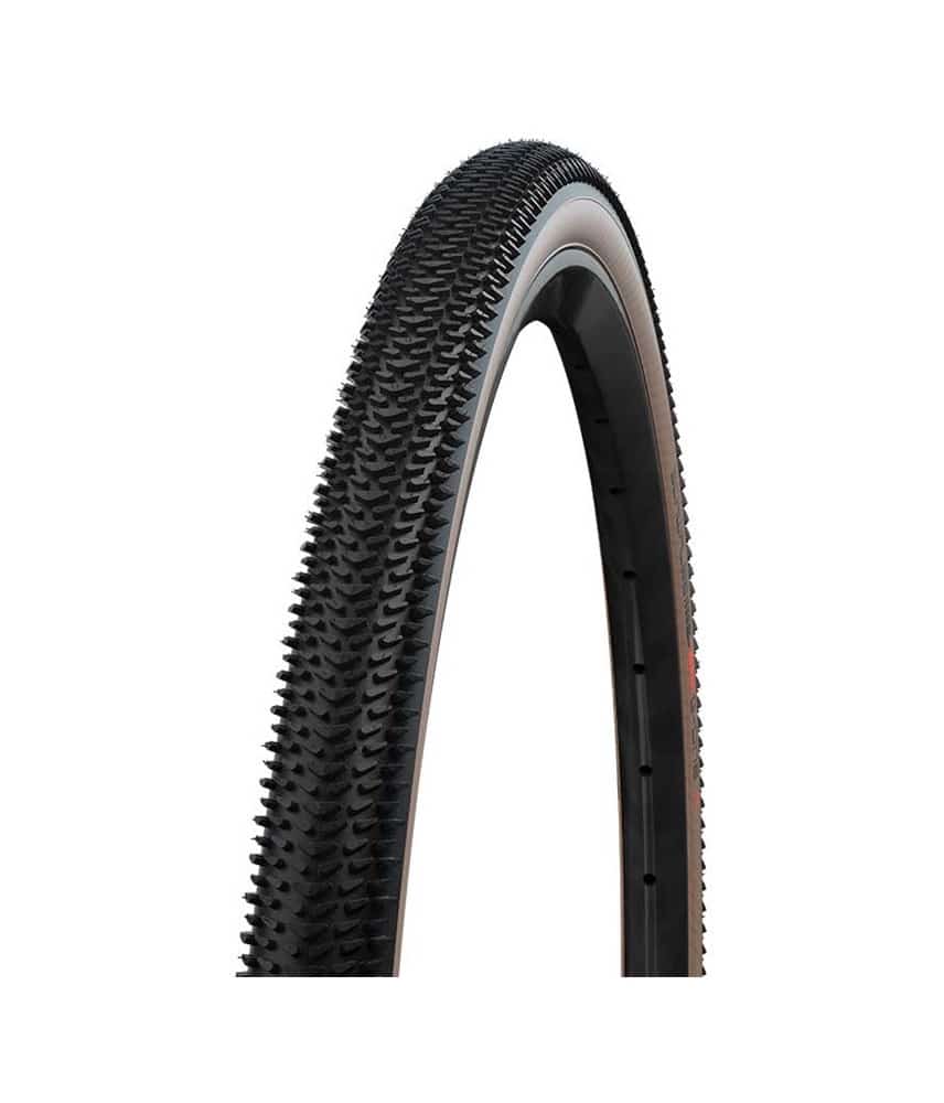 SCHWALBE-G-One-R-brun.jpg Ett hopfällt Schwalbe G-ONE R EVO 40-622mm graveldäck i brun och svart. Däcket har ett grovt mönster för bra grepp, med en ljus bakgrund som framhäver detaljerna.
