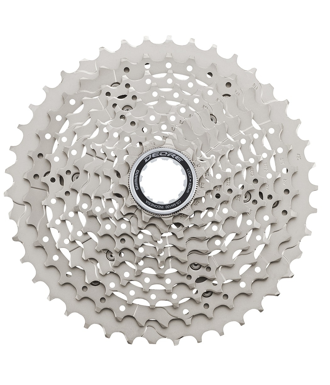 Shimano-Deore-10-CSM4100.jpg Detaljerad bild av en Shimano Deore CS-M4100 kassett, 10-växlad, i silverfärg. Stark belysning framhäver de intrikata detaljerna och den tekniska designen. Fokus på växelkombinationerna och Shimano-logotypen.