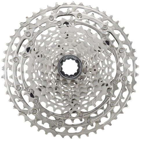 Silverfärgad Shimano Deore CS-M5100 11-växlad kassett, fotograferad i starkt ljus mot en vit bakgrund. Detaljerade kuggar och texten på låsringen är väl synliga.