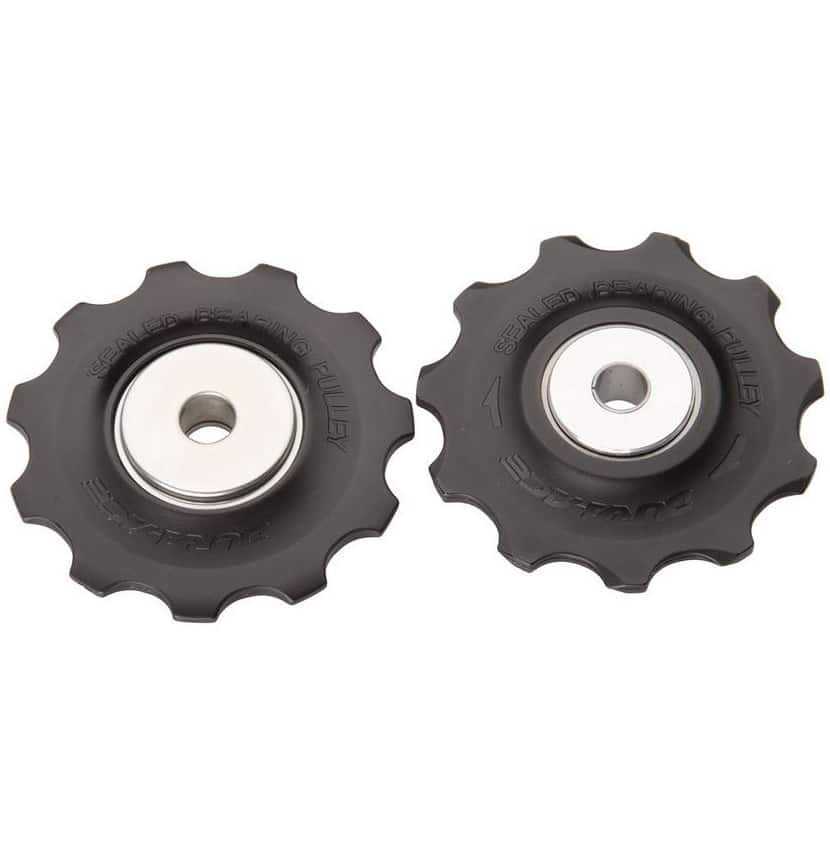Shimano-Dura-Ace-RD-7900-rulltrissor.jpg Två Dura Ace RD-7900 rulltrissor för bakväxel, avbildade i detalj med skarp fokus på "SEALED BEARING PULLEY"-texten och silverfärgade centrum. Neutral bakgrund ger klarhet.