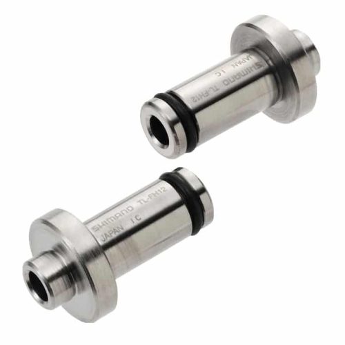Två Shimano TL-FH12-adaptrar för 12 mm genomgående axelnav visas i detalj. Metalliska och cylindriska, de har svarta gummiringar och är märkta med "SHIMANO TL-FH12 JAPAN IC". Ljuset är klart och fokuserat.