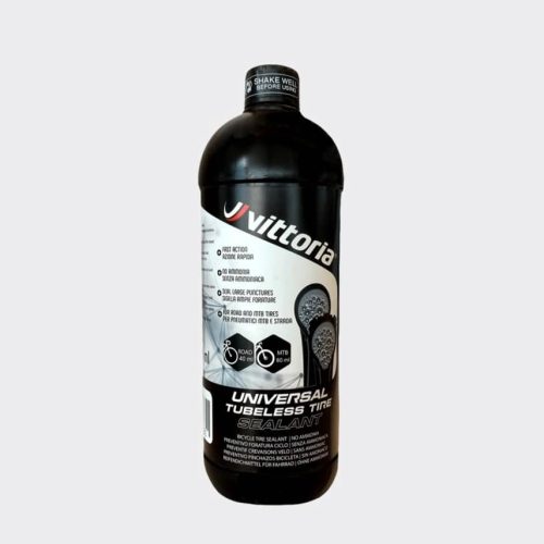 En flaska Vittoria Pit Stop tubelessvätska står mot en ljusgrå bakgrund. Flaskan är svart med vit text och ikoner som beskriver produktens egenskaper, inklusive dess användning för både racer- och mountainbikedäck.