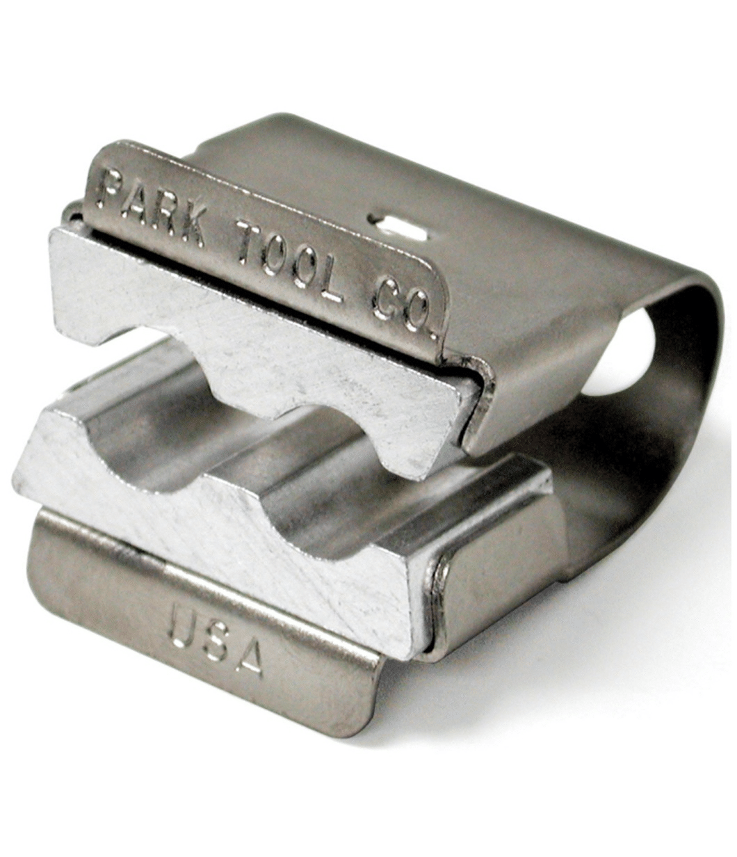 axelhallare-park-tool.png Silverfärgad axelhållare från Park Tool, AV-1, för skruvstäd. Metallisk glans under stark belysning framhäver detaljerna och graveringarna 'Park Tool Co.' och 'USA'.