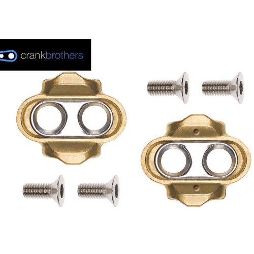 Två Crankbrothers pedalklossar i mässing och silver med tillhörande skruvar, presenterade mot en vit bakgrund. Studioljus framhäver detaljerna och den sex graders rörligheten.