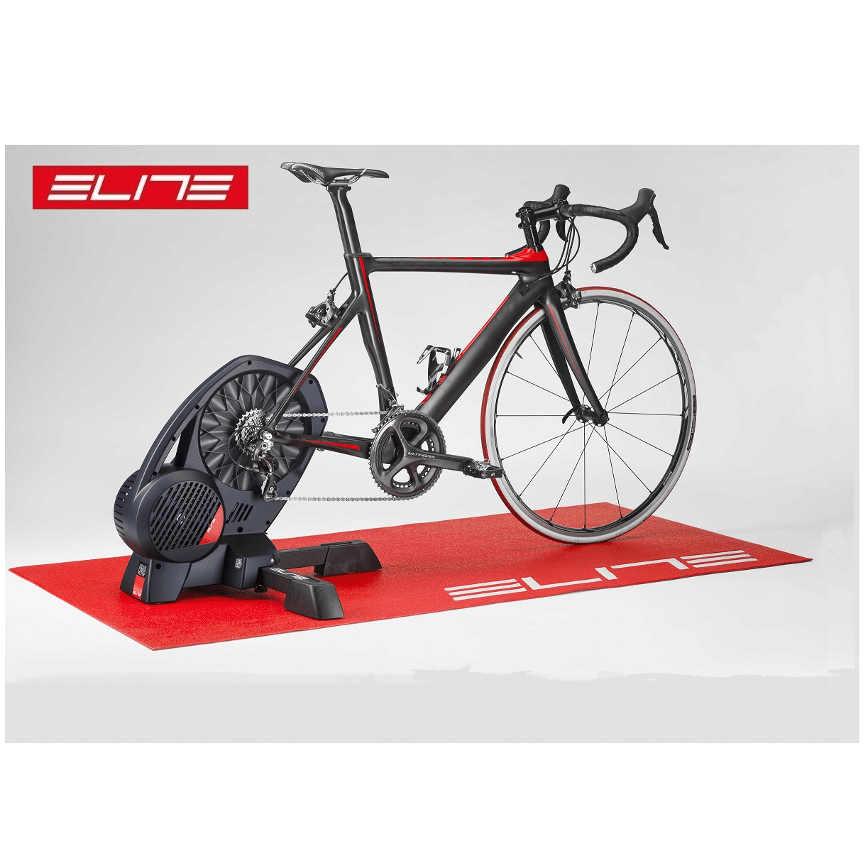 elite.trainer.matta_.png En cykel på en röd Elite-träningsmatta i en ljus studio. Mattan har vita ränder och Elite-logotypen. Atmosfären är ren och professionell, med fokus på produkterna.