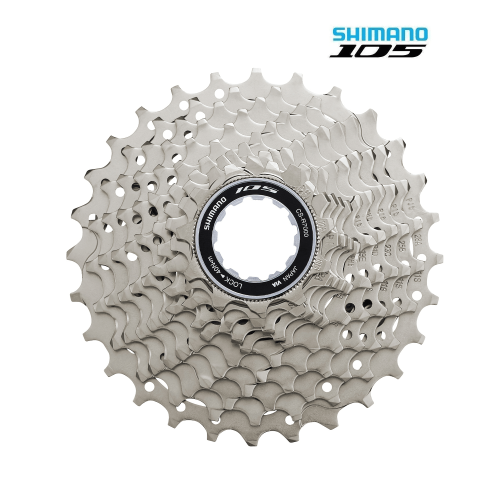 Silvrig Shimano 105 CS-R7000-11 kassett dominerar mot vit bakgrund, med varumärkeslogotyp och modellbeteckning tydligt exponerade. Belysningen framhäver detaljerna i kuggkransarna.