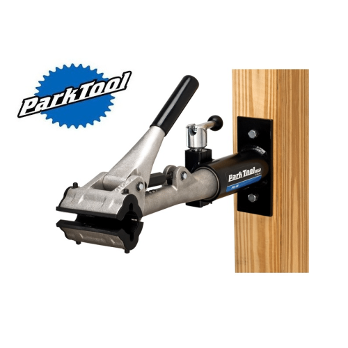 Park Tool PRS-4W-1 mekställ för vägg- eller stolpmontering. Silverfärgat verktyg med svart handtag och fastsättningsanordning monterad på en trästolpe. Studioljus framhäver detaljerna.