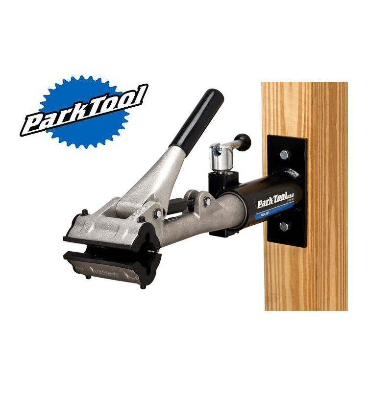 mekstall-stolpe.png Park Tool PRS-4W-1 mekställ för vägg- eller stolpmontering. Silverfärgat verktyg med svart handtag och fastsättningsanordning monterad på en trästolpe. Studioljus framhäver detaljerna.