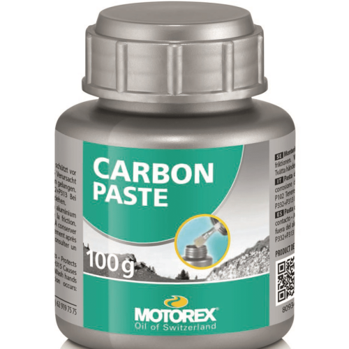 Ett burk Motorex Carbon Paste visas i en detaljerad produktbild. Burken, i silverfärg med grön etikett, står i ett ljust upplyst utrymme, vilket framhäver text och produktens dimensioner. Etiketten innehåller information om pastans användning och varumärket Motorex.