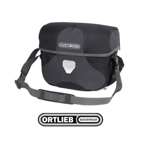 Ortlieb Ultimate Six Plus i i granit/svart är en vattentät axelremsväska med reflexer på framsidan, justerbar rem och Ortlieb-logotyp, mot en vit bakgrund.