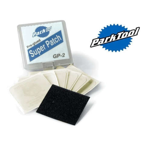Park Tool GP-2C reparationslappar ligger utspridda på en vit yta, tillsammans med sandpapper och en genomskinlig plastask med produktinformation i blått.