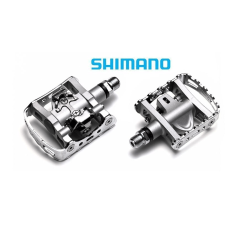 Två silverfärgade Shimano PD-M324 SPD-pedaler visas i detalj mot en vit bakgrund. Belysningen framhäver pedalernas konstruktion och material, vilket ger en ren och professionell produktbild.