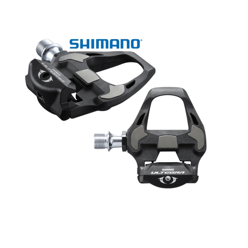 Shimano Ultegra PD-RD8000 SPD-SL pedaler visas i detalj under stark belysning, vilket framhäver den svarta finishen och de silverfärgade detaljerna. Logotypen är tydligt synlig ovanför pedalerna.
