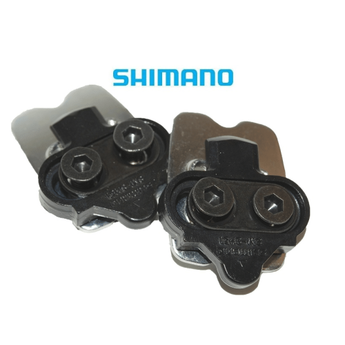 Detaljrik närbild av ett par Shimano SPD SM-SH51 pedalklossar med monteringsplatta. Klossarna är svarta och silverfärgade, placerade mot en vit bakgrund under starkt ljus.
